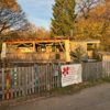 Blick auf das Gelände des Kinderladens an der Jugendfarm mit Zaun und Banner und Bauwagen im Hintergrund